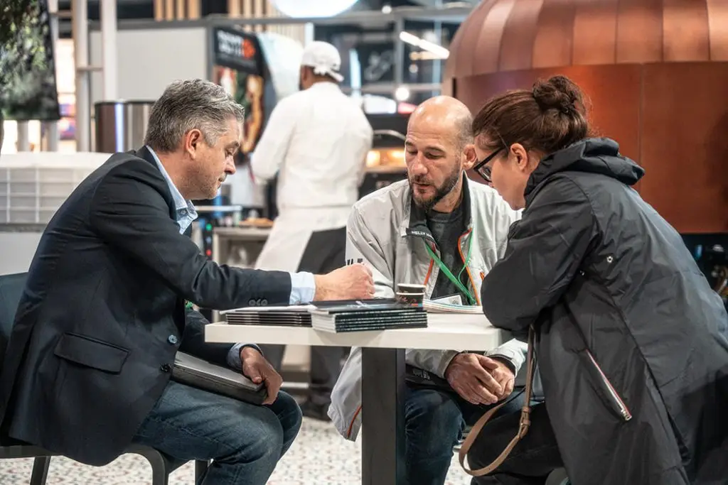 Photo de 3 personne discutant l'une d'entre elle écrivant quelle que chose que les autres regardes.