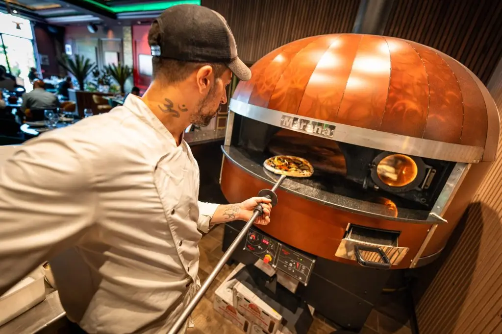 Photo d'une personne mettant une pizza dans une four a pizza Marana