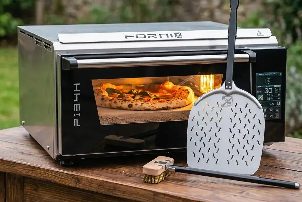 Four à pizza portable électrique Effeuno P134H posé sur une table en bois, avec une pizza en cuisson, une pelle perforée et une brosse