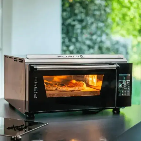 Four à pizza électrique portable Effeuno P134H avec une pizza en cuisson, devant un fond de verdure