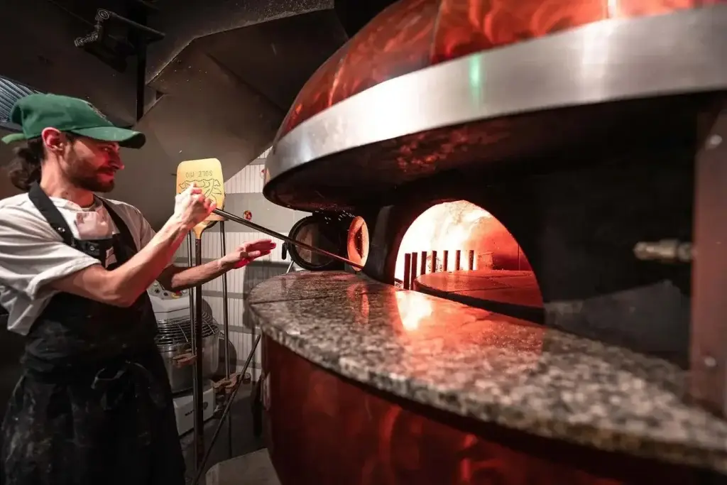Pizzaiolo enfournant une pizza dans un four à dôme cuivré Marana Forni